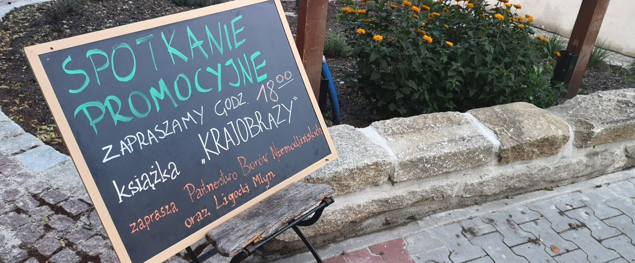 Szyld z informacją o spotkaniu promocyjnym związanym z wydaniem publikacji "Krajobrazy".